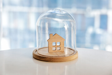 Wooden model of house under glass cap. Symbol of safe home. Insurance or protecting building...