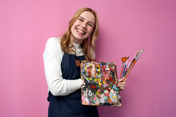 happy girl artist with drawing equipment laugh on a pink background, funny student of art school