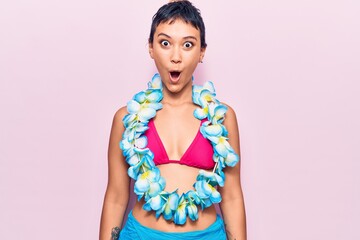 Young woman wearing bikini and hawaiian lei scared and amazed with open mouth for surprise,...