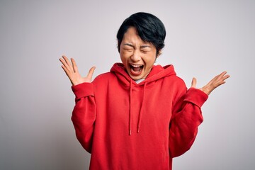 Young beautiful asian girl wearing casual sweatshirt with hoodie over white background celebrating mad and crazy for success with arms raised and closed eyes screaming excited. Winner concept