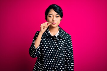 Young beautiful asian girl wearing casual jacket standing over isolated pink background mouth and...