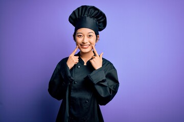 Young beautiful chinese chef woman wearing cooker uniform and hat over purple background Smiling...