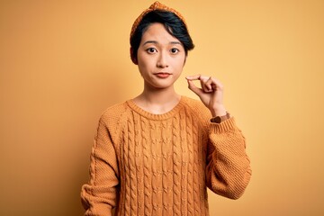 Young beautiful asian girl wearing casual sweater and diadem standing over yellow background mouth...