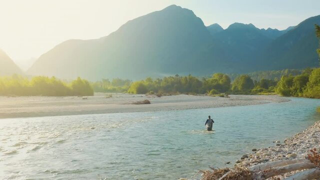 Aerial shot of a man using the flyfishing technique to catch fish in a running river during sunset