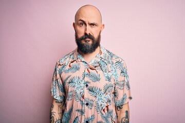 Handsome bald man with beard and tattoo wearing casual floral shirt over pink background skeptic and nervous, frowning upset because of problem. Negative person.