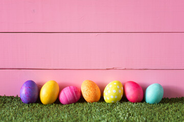 Colorful Easter Eggs in Row on Bottom of Pink Wood Boards Wall Background and Laying in Green Grass with room or space for copy.