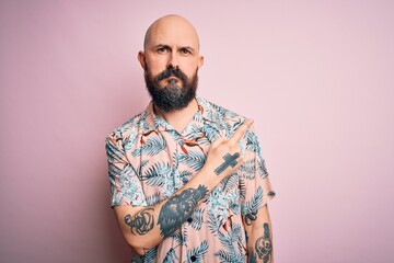 Handsome bald man with beard and tattoo wearing casual floral shirt over pink background Pointing with hand finger to the side showing advertisement, serious and calm face