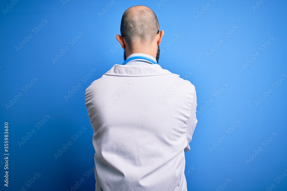 Poster handsome bald doctor man with beard wearing glasses and stethoscope over blue background standing ba