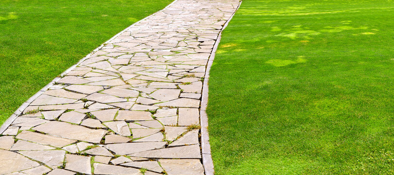 flagstone footpath in a park with a green lawn goes into perspective on a sunny summer day, closeup of brown paving stone tiles with copy space 16:9.