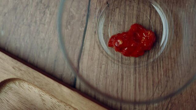 A measure of 1 TBSP of Chilli paste in a transparent glass bowl on a brown wooden table. Rotating camera capturing a food ingredient.