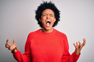 Young beautiful African American afro woman with curly hair wearing red casual sweater crazy and mad shouting and yelling with aggressive expression and arms raised. Frustration concept.