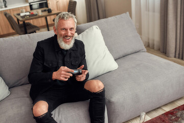 Stay on top. Bearded middle-aged man holding controller, playing video games after smoking...