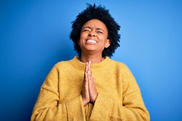 Young beautiful African American afro woman with curly hair wearing yellow casual sweater begging and praying with hands together with hope expression on face very emotional and worried. Begging.