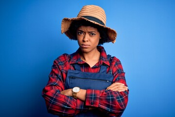 Young African American afro farmer woman with curly hair wearing apron and hat skeptic and nervous, disapproving expression on face with crossed arms. Negative person.