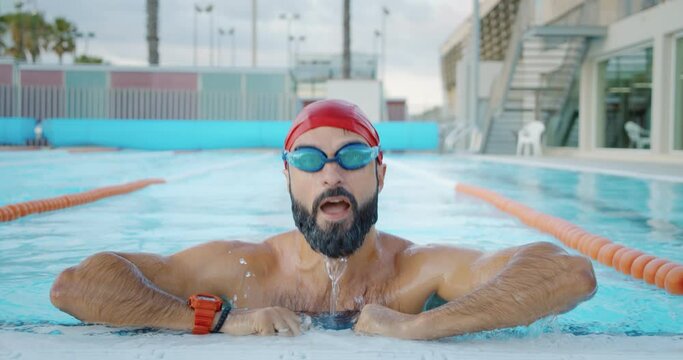 Bearded muscular swimmer coming up of the olympic swimming pool after his morning training. Slow motion close-up 4k video
