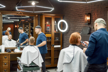 Usual day at barbershop. Two barbers working with clients in the modern barbershop