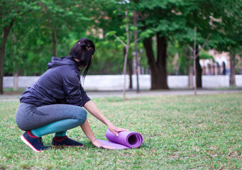 Beautiful    girl untwists the mat and preparing for  gymnastics and stretching  in the park.  Concept of sport