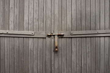Wings of a gray, wooden gate closed with a padlock