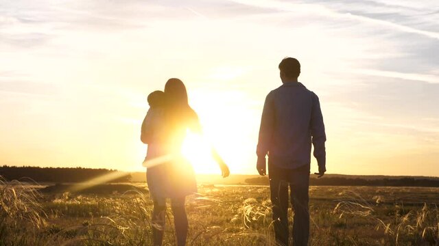 free family mom dad and little daughter walks in field at sunset holding hands. healthy happy baby sleeping in mother s arms. The concept of family and children.