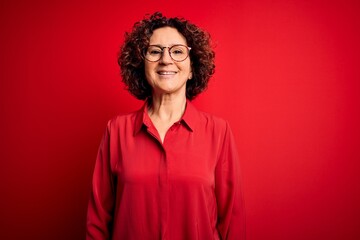 Fototapeta na wymiar Middle age beautiful curly hair woman wearing casual shirt and glasses over red background with a happy and cool smile on face. Lucky person.