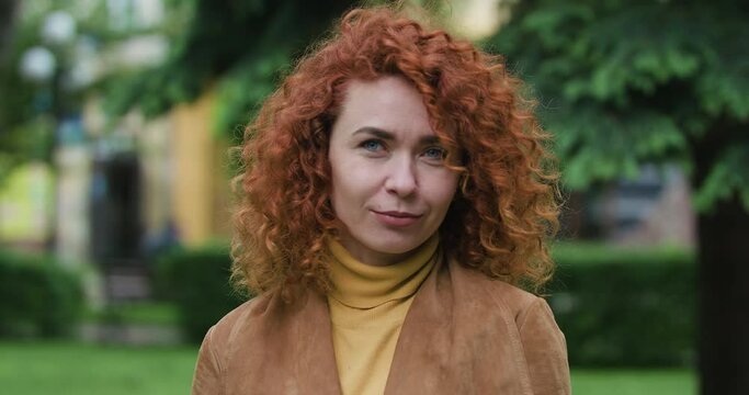 Attractive red-haired woman with curly hair looks at the camera and says something, close up slow motion
