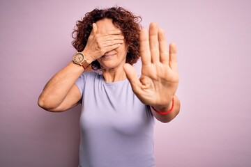 Middle age beautiful curly hair woman wearing casual t-shirt over isolated pink background covering eyes with hands and doing stop gesture with sad and fear expression. Embarrassed and negative