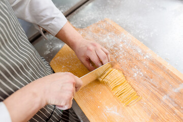 Cut noodles on kitchen . Chef cooks spaghetti in restaurant. Chef cuts with a knife raw noodles with flour. Cooking ramen soup