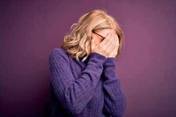 Middle age beautiful blonde woman wearing casual purple turtleneck sweater and glasses with sad expression covering face with hands while crying. Depression concept.