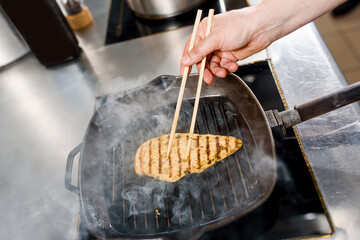 Fried chicken fillet in a pan. Cooking ramen soup. Chef touches chicken with a japanese sticks for food.