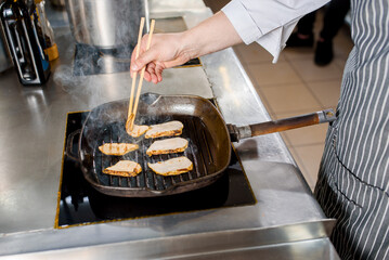 Fried chicken pieces of fillet in a pan. Cooking ramen soup. Chef touches chicken with a japanese sticks for food.