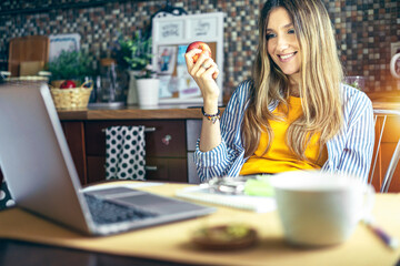 Distance learning online education and work. Woman with apple having a video call. Happy and smiling girl working from kithcen home office. Using computer and watch movies and online shops.