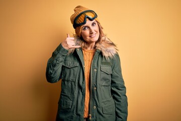 Middle age beautiful blonde skier woman wearing snow sportwear and ski goggles smiling doing phone gesture with hand and fingers like talking on the telephone. Communicating concepts.