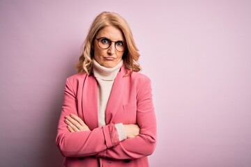 Obraz premium Middle age beautiful blonde business woman wearing elegant pink jacket and glasses skeptic and nervous, disapproving expression on face with crossed arms. Negative person.