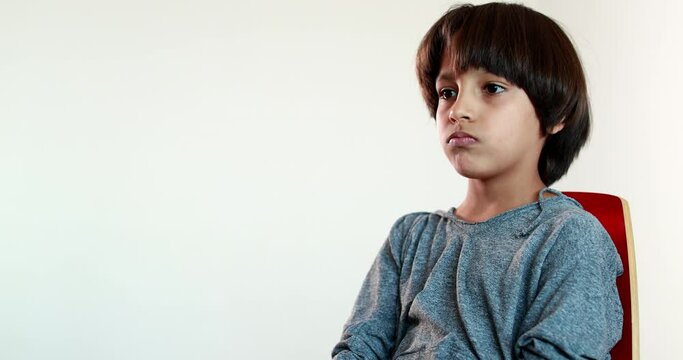 Pensive child boy sitting on chair thinking, kid crossing arms feeling upset emotion