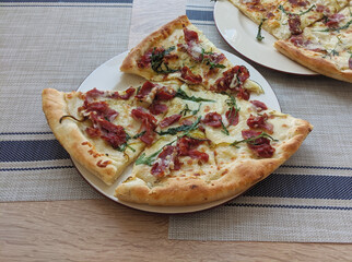 Pizza with prosciutto, hot sticky cheese and arugula salad leaves served sliced on plate
