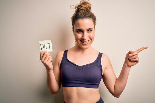 Young beautiful blonde sportswoman wearing sportswear holding reminder with diet message very happy pointing with hand and finger to the side