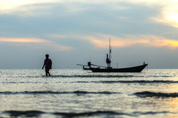 Naklejka premium silhouette of a man walking and fishing Boat in the sea at sunset