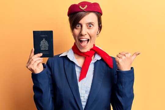 Young beautiful woman wearing stewardess uniform holding canadian passport pointing thumb up to the side smiling happy with open mouth