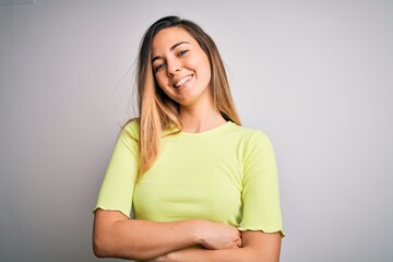 Fototapeta premium Beautiful blonde woman with blue eyes wearing green casual t-shirt over white background happy face smiling with crossed arms looking at the camera. Positive person.