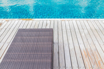 swimming pool in the hotel resort with weaving bench on wooden floor during beautiful sunny day in summer season