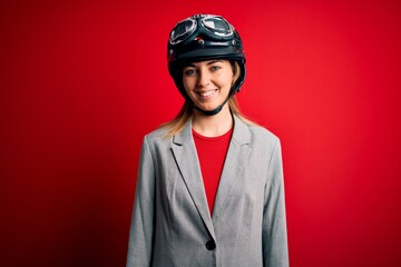 Young beautiful blonde motorcyclist woman wearing motorcycle helmet over red background with a happy and cool smile on face. Lucky person.