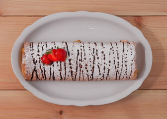 Sponge cake with tea on a wooden table.
One biscuit roll in a white plate lies on a wooden table  close-up.