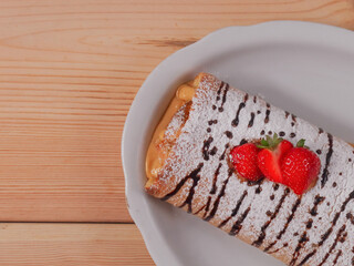 Sponge cake with tea on a wooden table.
One slice of biscuit roll in a white plate licks on a wooden table, close-up and with place for text on the left.