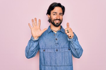 Fototapeta premium Young handsome hispanic bohemian man wearing hippie style over pink background showing and pointing up with fingers number six while smiling confident and happy.