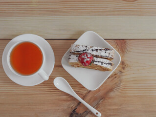 Sponge cake with tea.
One slice of biscuit roll and a mug of black tea on a wooden table, closeup