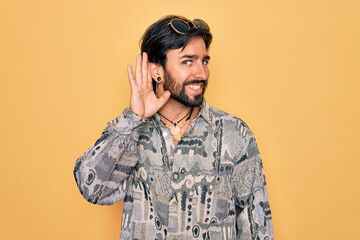 Young handsome hispanic bohemian man wearing hippie style and sunglasses smiling with hand over ear listening an hearing to rumor or gossip. Deafness concept.