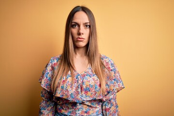 Young beautiful blonde woman with blue eyes wearing summer clothes over yellow background with serious expression on face. Simple and natural looking at the camera.