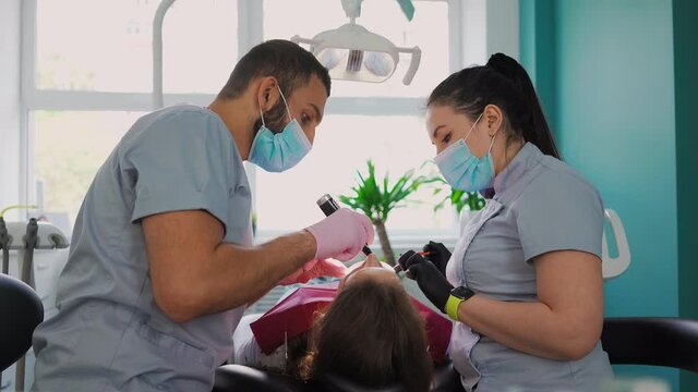 Two dentist doctors in medical masks, a man and a woman in a dental office, perform an operation on the teeth. Dentistry. Healthcare and Medicine Concept. Slow motion