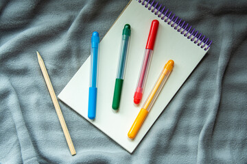 A notebook with pencil, color markers on a gray plaid background. Cosy workspace. Top view, flat lay