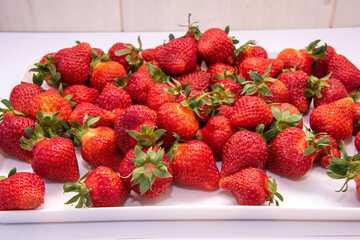 tasty strawberries in a white tray on a wooden background. Close-up